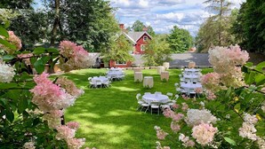 A well-maintained outdoor garden with neatly arranged round tables and chairs, surrounded by lush greenery and flowering plants. - Springside Inn (Auburn)