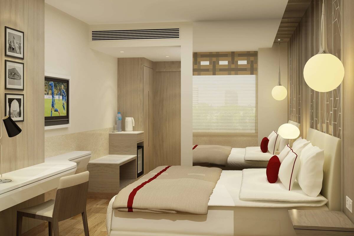 Ein modernes Hotelzimmer mit Schreibtisch, zwei Betten, einem kleinen Tisch und einem Fenster mit Jalousien.