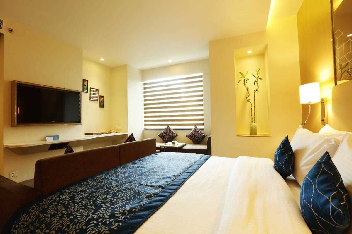 Ein Hotelzimmer mit Bett, Schreibtisch, Fernseher und einem Fenster mit Jalousien.