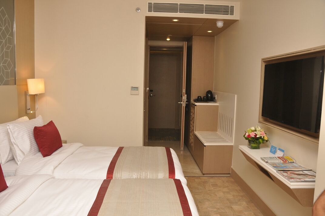 A hotel room with two beds, a desk with a computer, a TV, and a small table with a vase of flowers.
