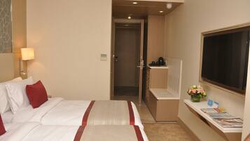 A hotel room with two beds, a desk with a computer, a TV, and a small table with a vase of flowers.