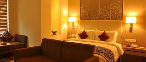 A hotel room with a bed, two bedside tables, a sofa, and a wall-mounted lamp.