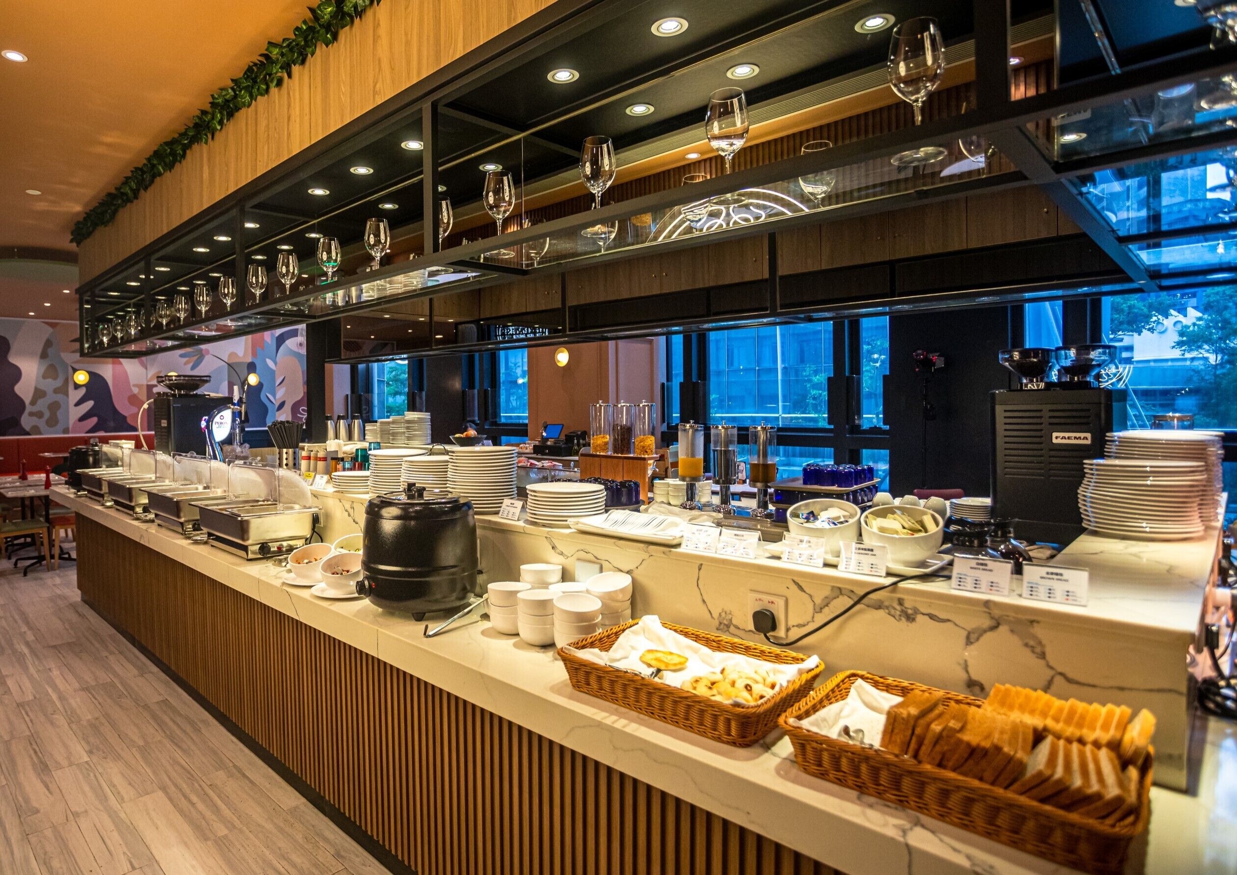 A buffet counter with various food items, a coffee machine, and a wine glass display.