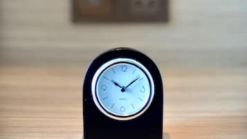 Een klok met een zwarte omlijsting en een witte wijzerplaat, waarop 'QUARTZ' staat, op een voetstuk.