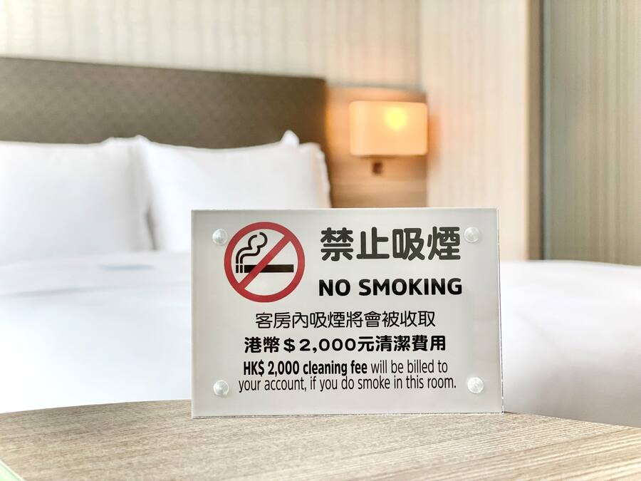 A no smoking sign in a hotel room with a bed and a nightstand with a lamp.