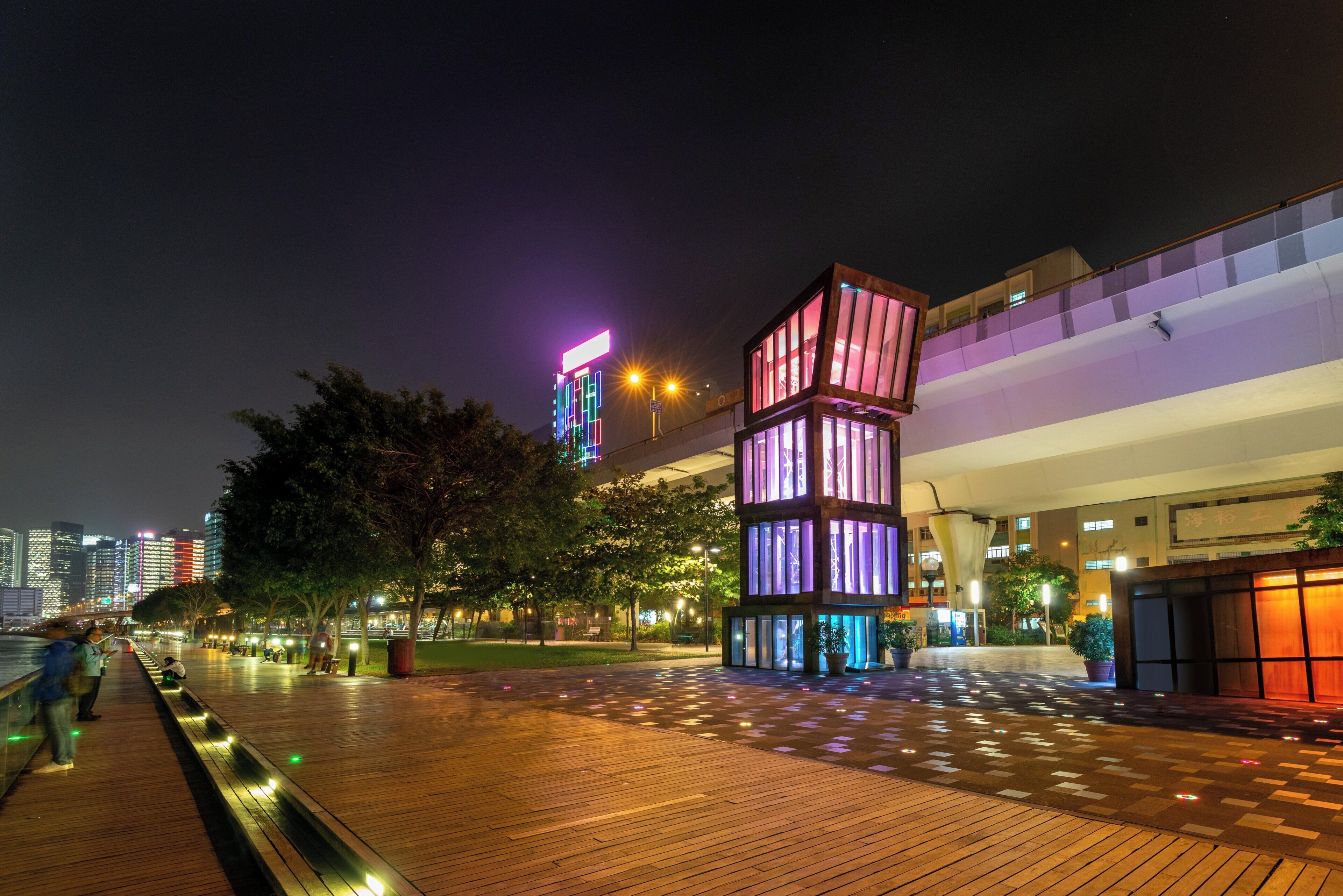 A nighttime urban scene with a modern building featuring illuminated windows and a unique geometric design.