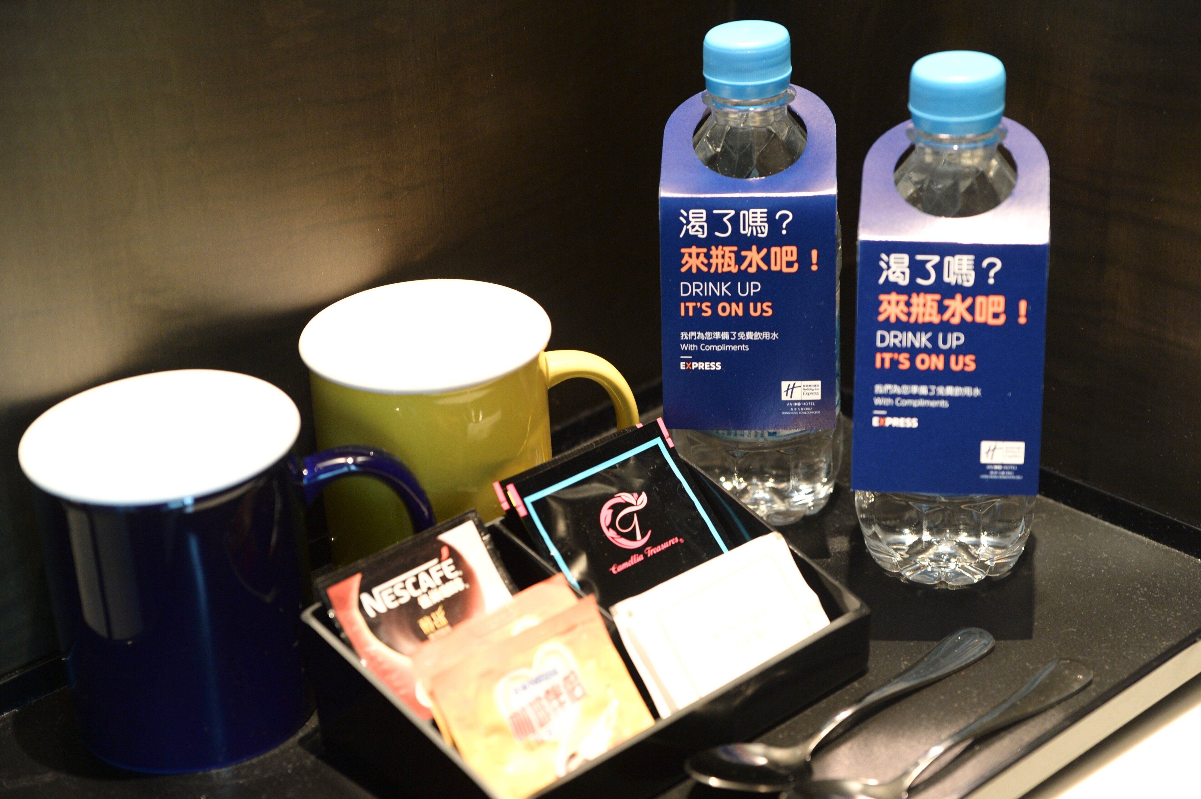A tray with a blue mug, a yellow mug, two water bottles, a card, and a spoon.