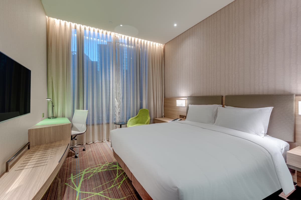A modern hotel room with a large bed, a desk, a chair, and a TV.