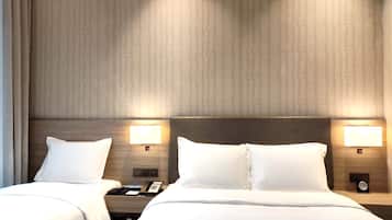 A hotel room with two beds, a nightstand with a phone, and wall-mounted lamps.