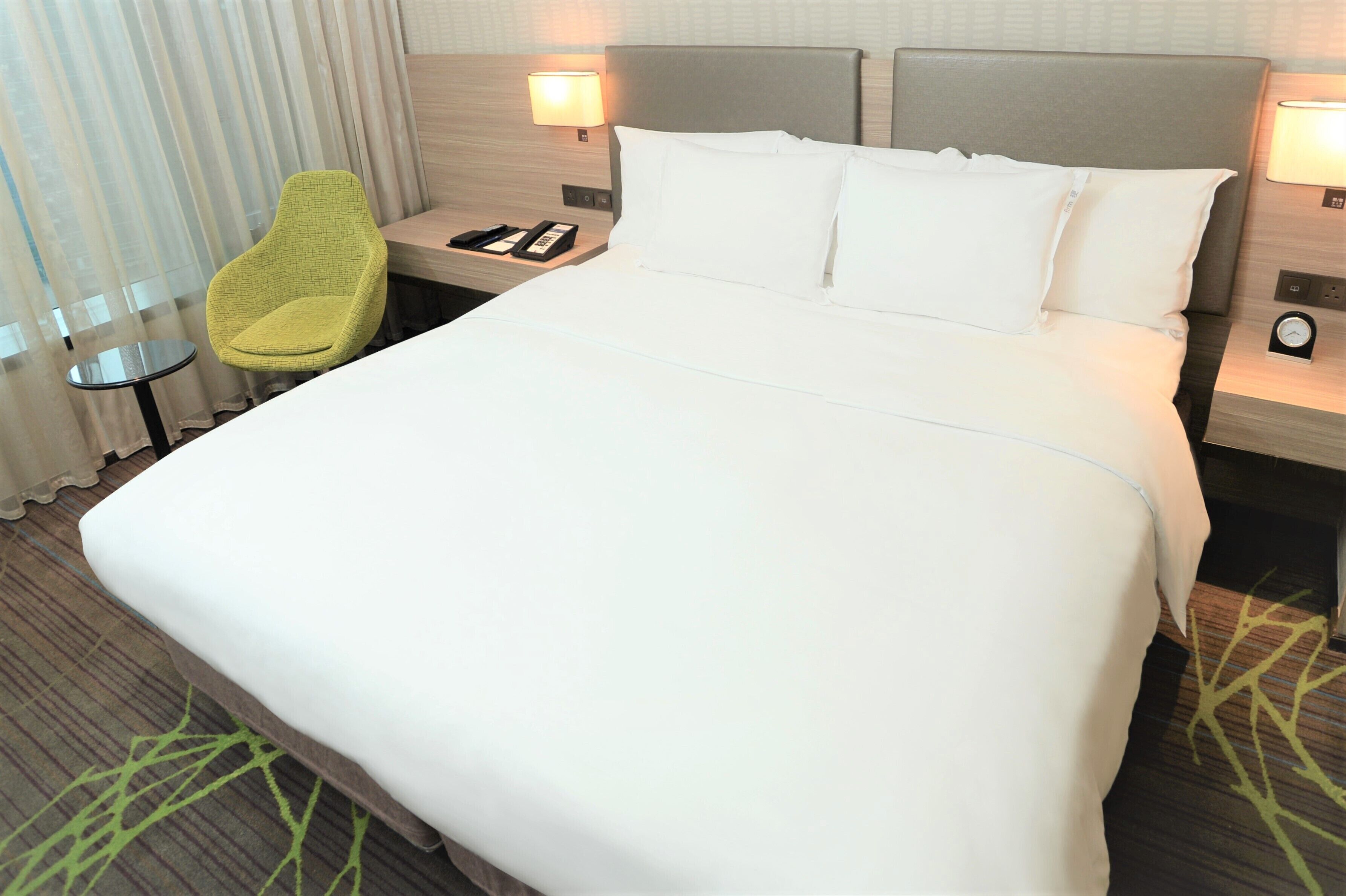 Habitació d'hotel amb un llit gran, dues taules de nit, una cadira i una làmpada.