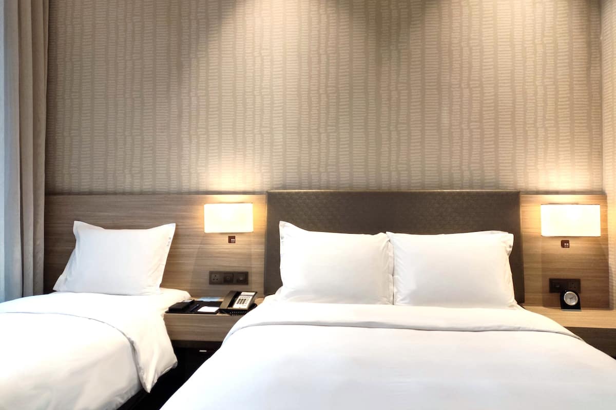 A hotel room with two beds, a nightstand with a phone, and wall-mounted lamps.