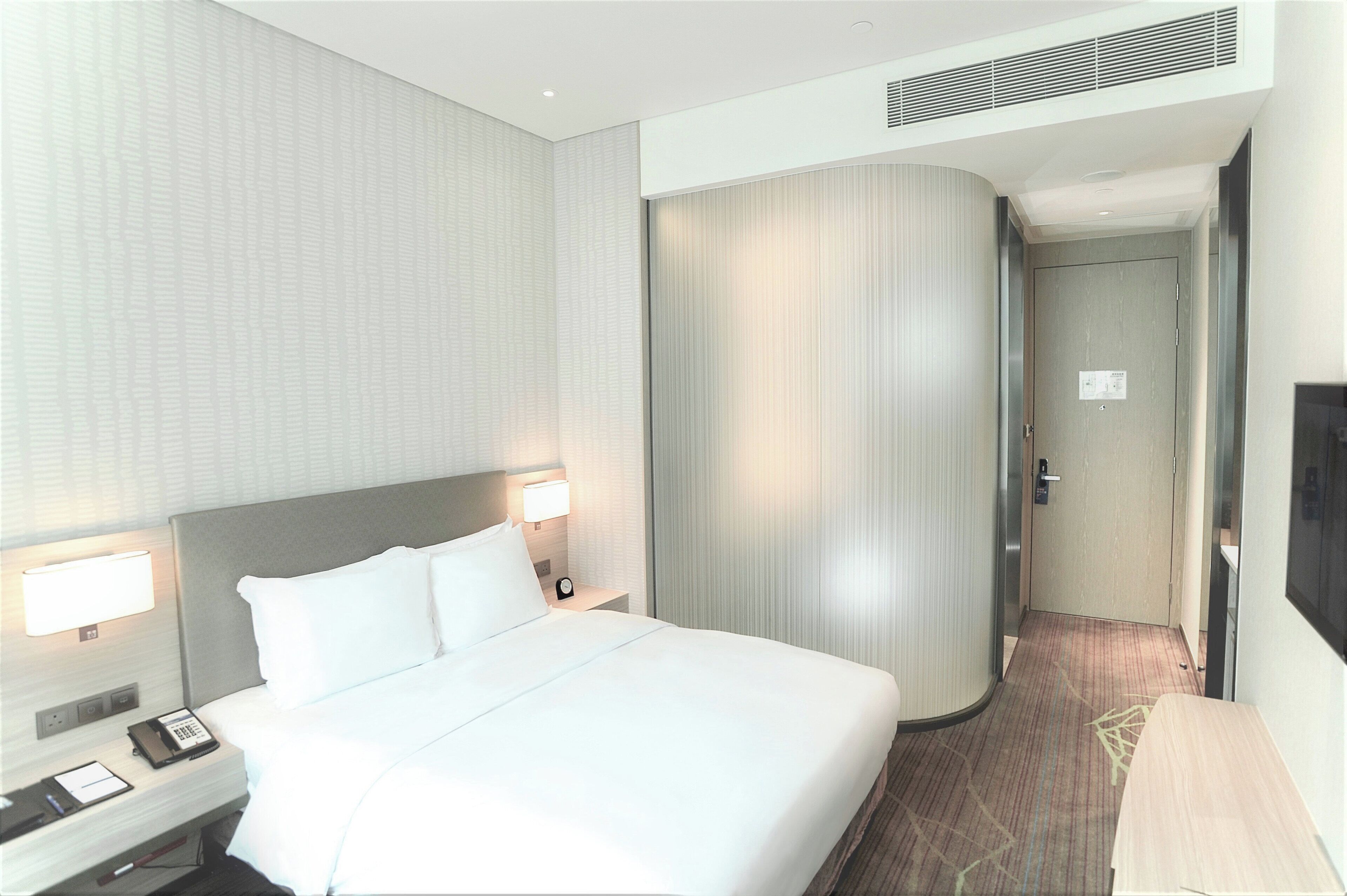 Una habitación de hotel con una cama grande, lámparas de noche, un teléfono y un televisor de pantalla plana.