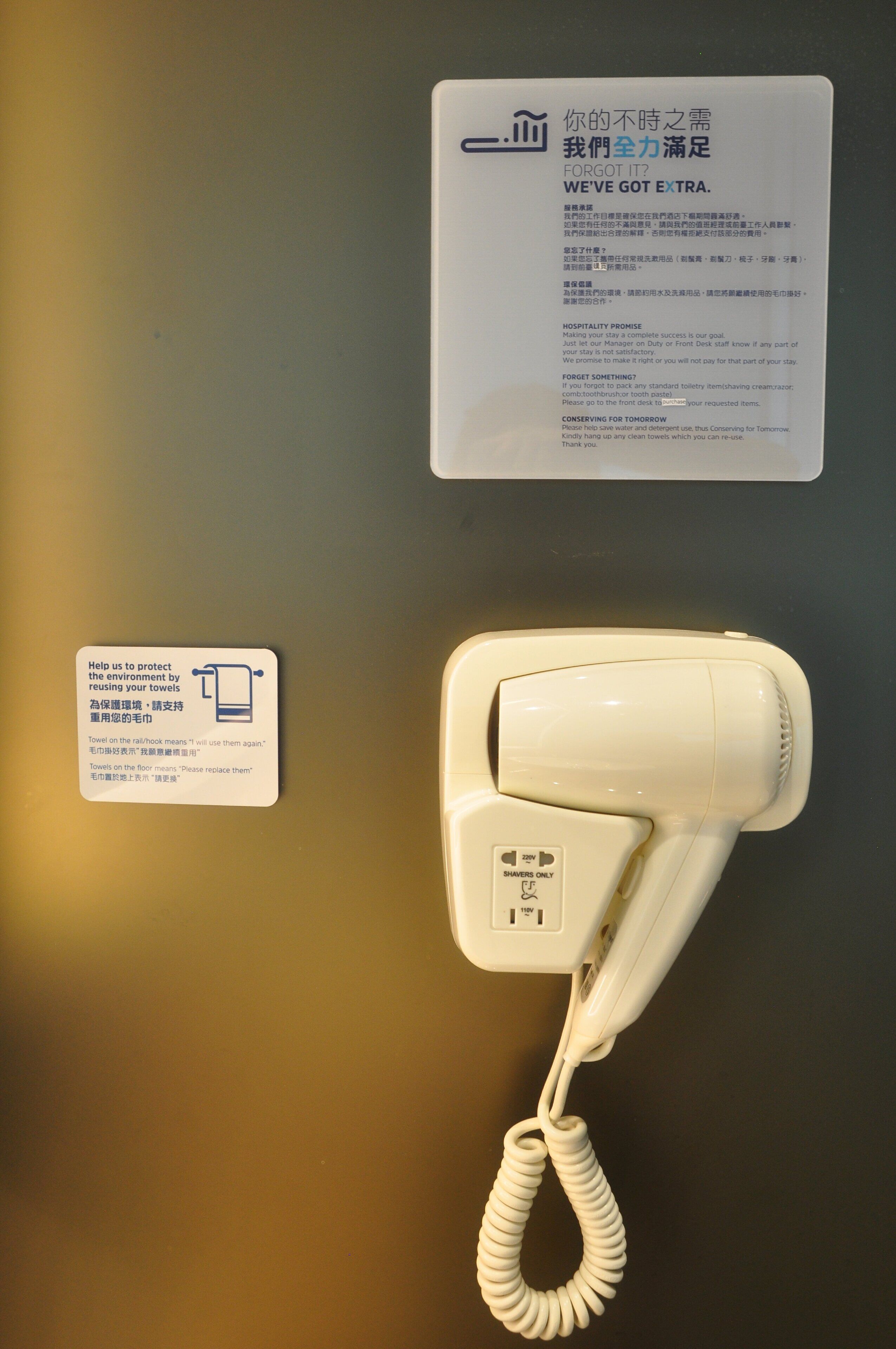 A hotel room with a white hairdryer and a sign about towel reuse.