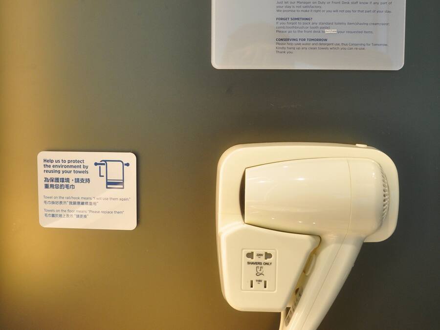 A hotel room with a white hairdryer and a sign about towel reuse.