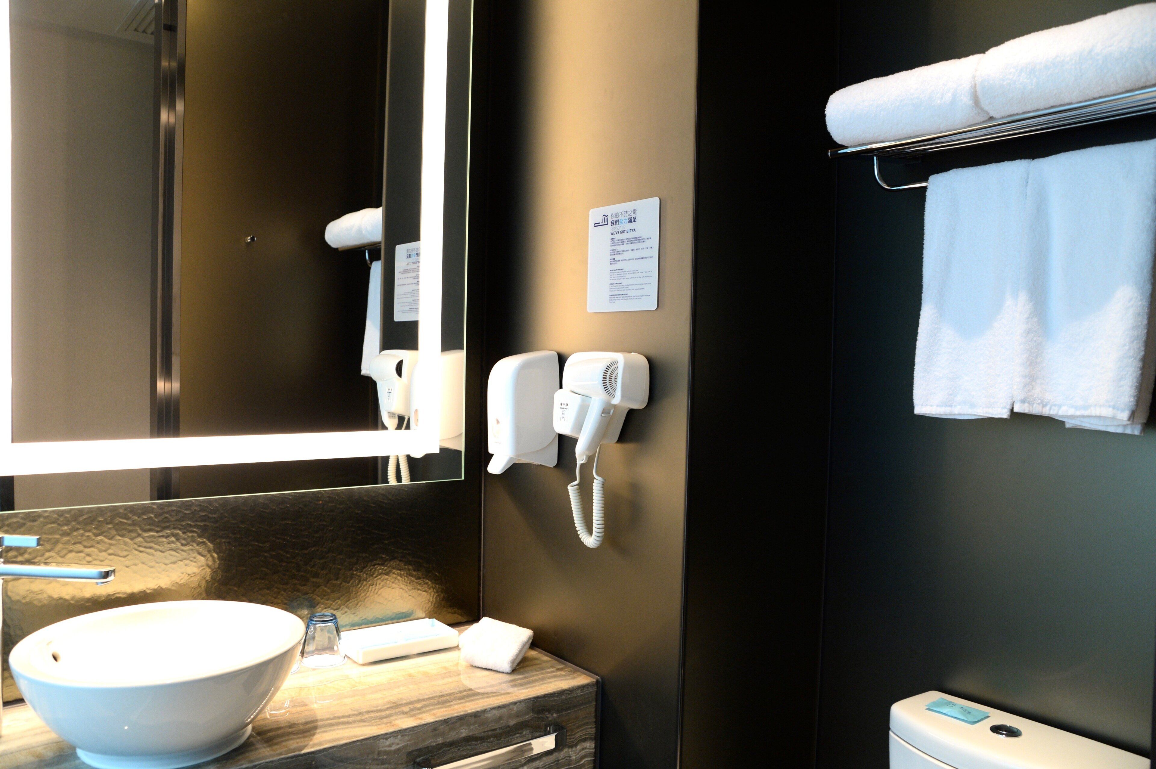A bathroom with a large mirror, a sink with a bowl, a hairdryer, and a towel rack with towels.