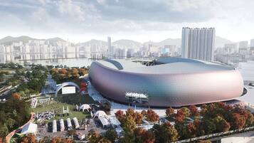 A modern stadium with a unique dome structure, surrounded by a landscaped area with trees and pathways.