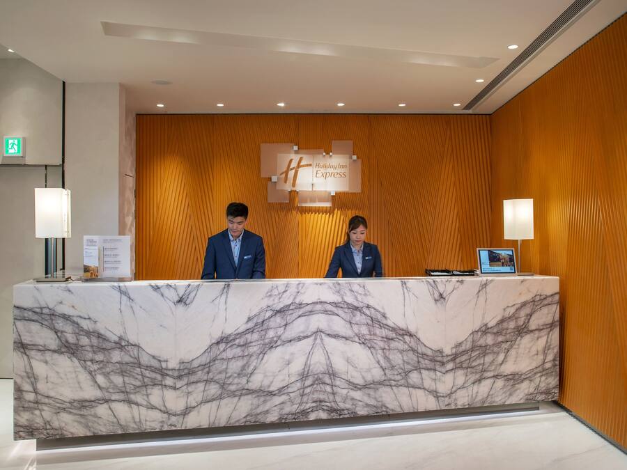 A reception desk with a marble top, two staff members, a wooden wall, and a sign for Holiday Inn Express.