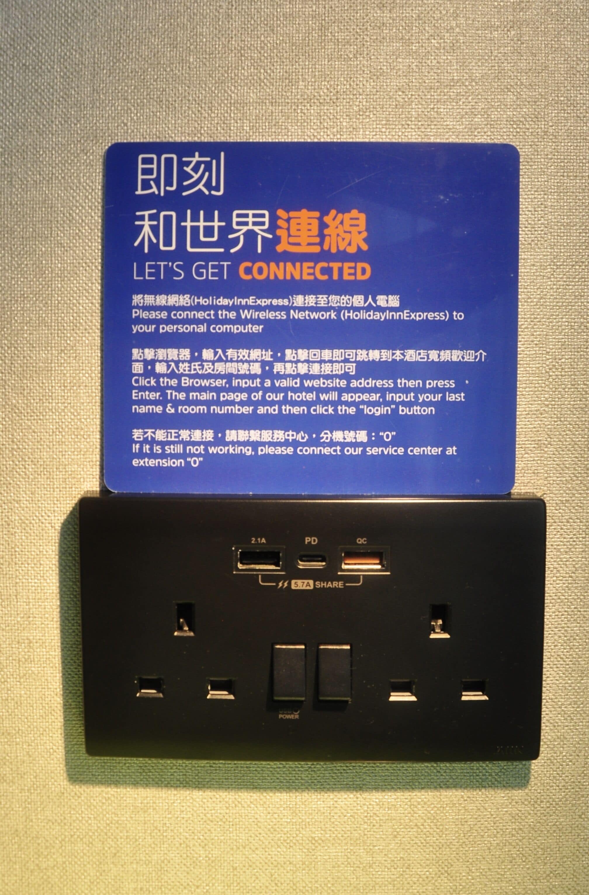 Een blauw bord met instructies voor het verbinden met het draadloze netwerk, geplaatst boven een stopcontact met meerdere USB-poorten en een schakelaar.