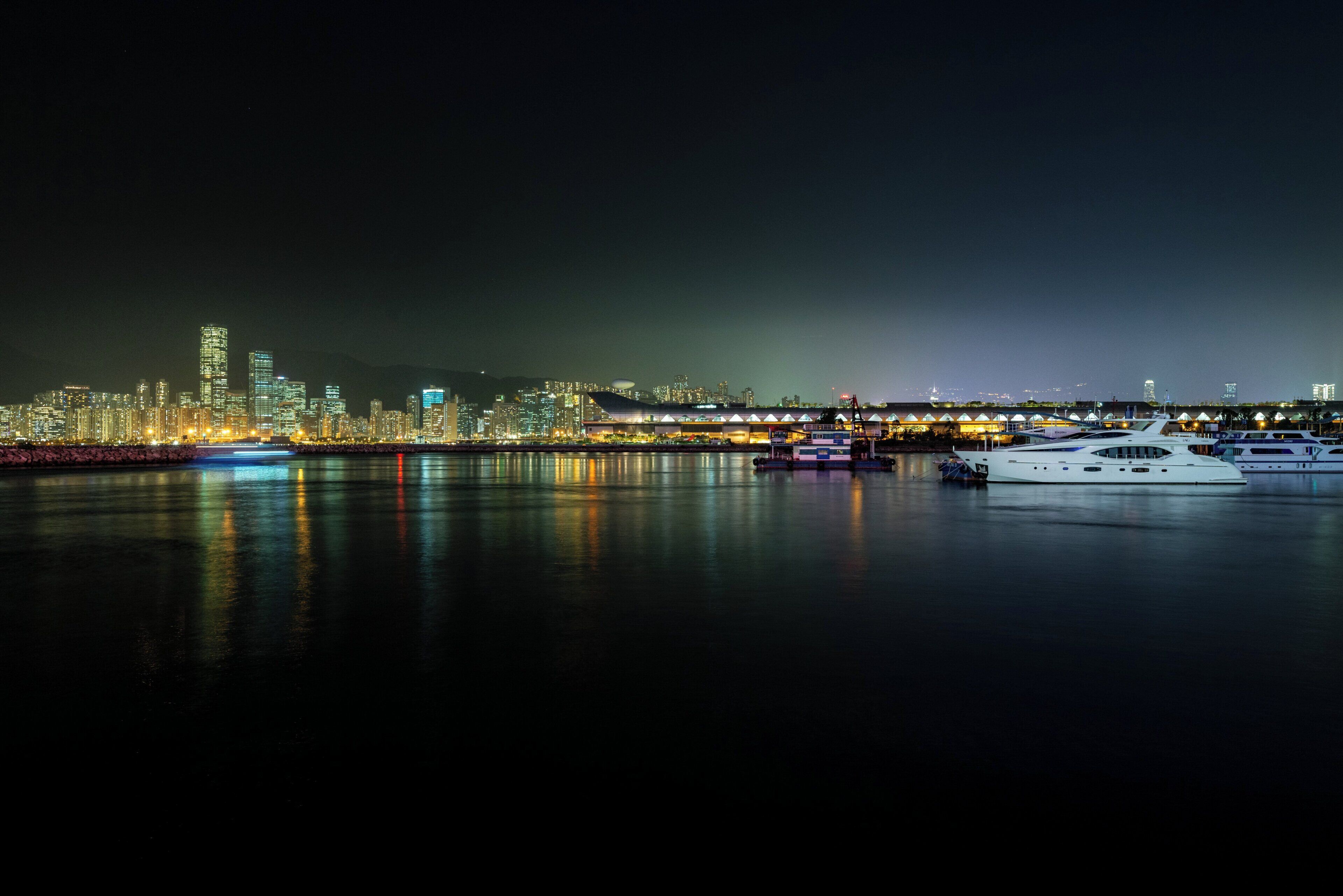 A nighttime cityscape with illuminated buildings and a marina with yachts.