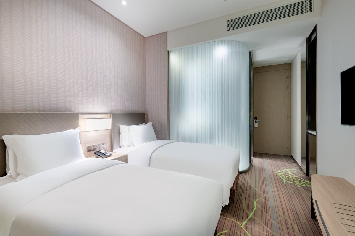 A hotel room with two beds, a nightstand with a phone, a large mirror, and a TV.