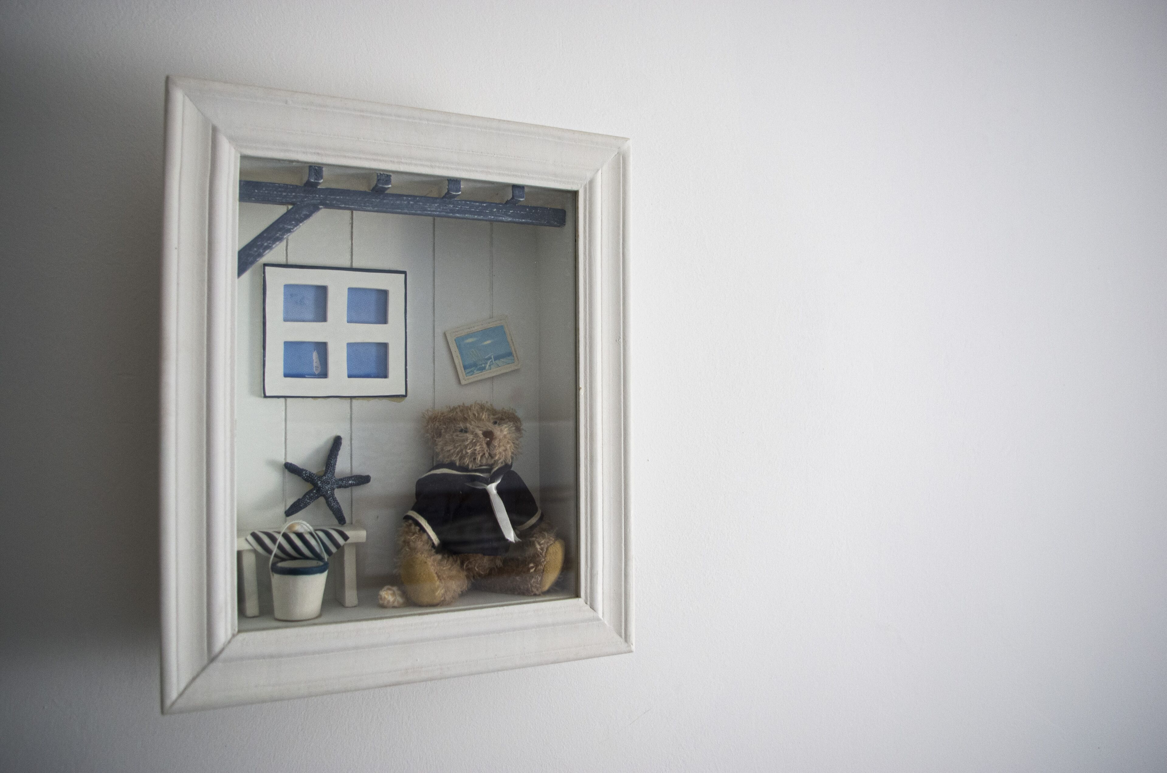 A framed display with a teddy bear, a starfish, a small chair, and a picture frame.