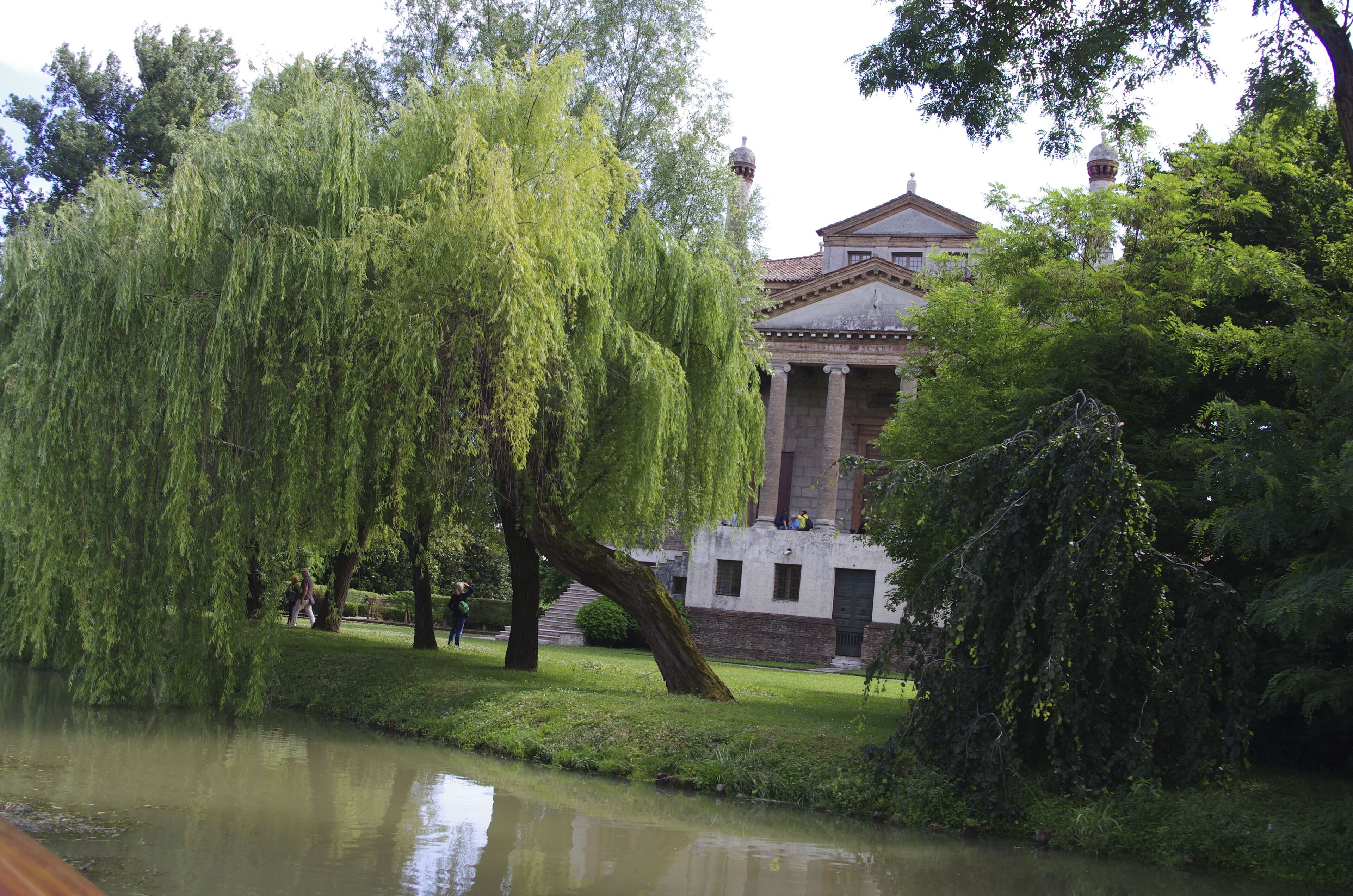 A classical building with columns, a pond, and weeping willow trees.