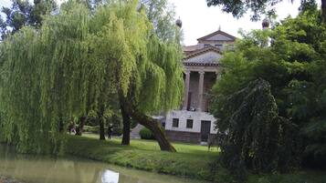 A classical building with columns, a pond, and weeping willow trees.
