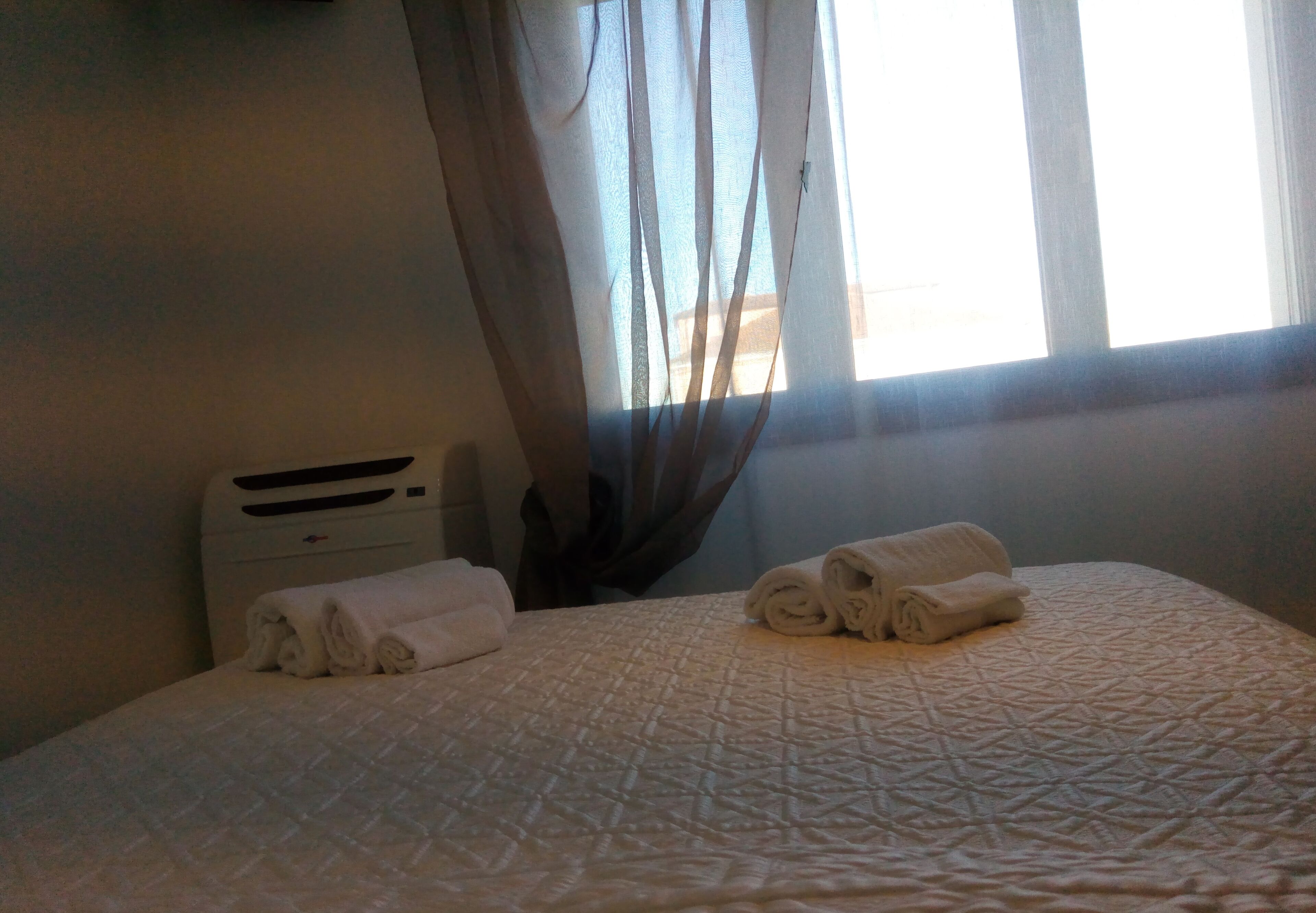 Una habitación de hotel con cama, calefactor y ventana con cortinas.