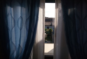 Vista a través de una ventana con cortinas estampadas, que muestra un edificio con tejado de baldosas y un pequeño jardín.