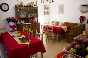 Un comedor con sillas y mesas de madera cubiertas con manteles rojos, un armario de madera con puertas de cristal y un reloj en la pared.