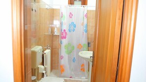 A small bathroom with two toilets, a sink, and a shower curtain with floral patterns. - Le Stanze di Lucia (Tricase)