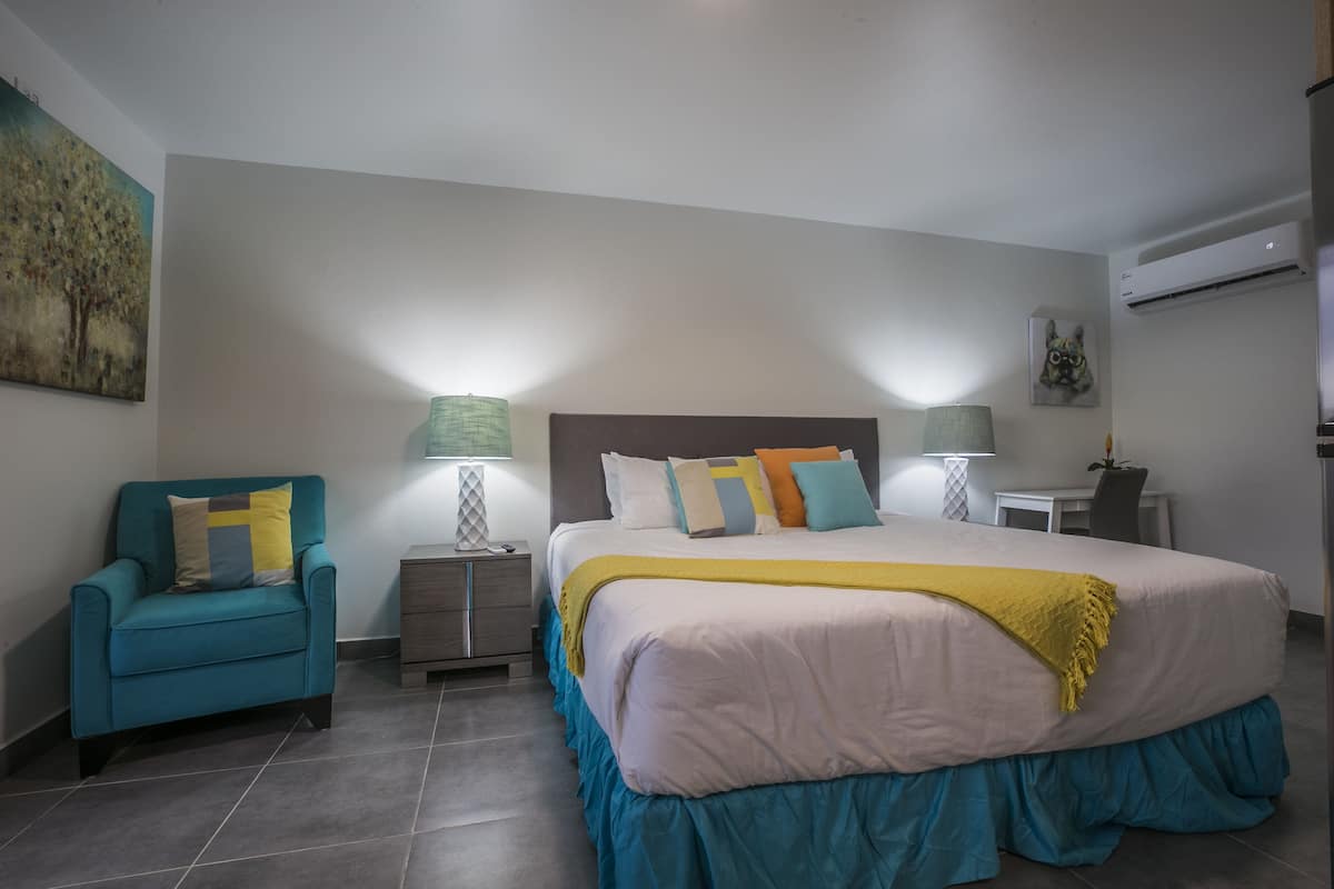 Quarto com cama, cadeira, mesa de cabeceira, escrivaninha e ar condicionado.
