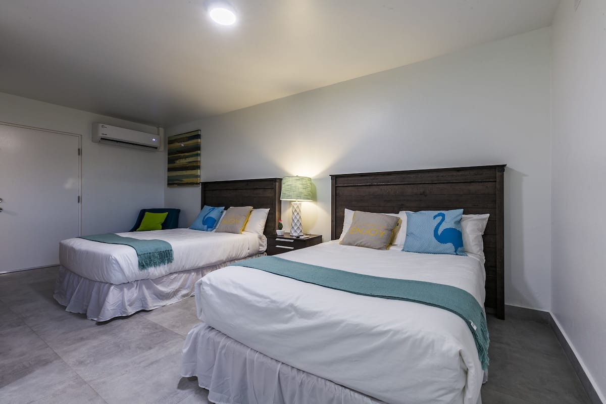 Quarto de hotel com duas camas, uma mesa de cabeceira, uma luminária e um aparelho de ar condicionado.