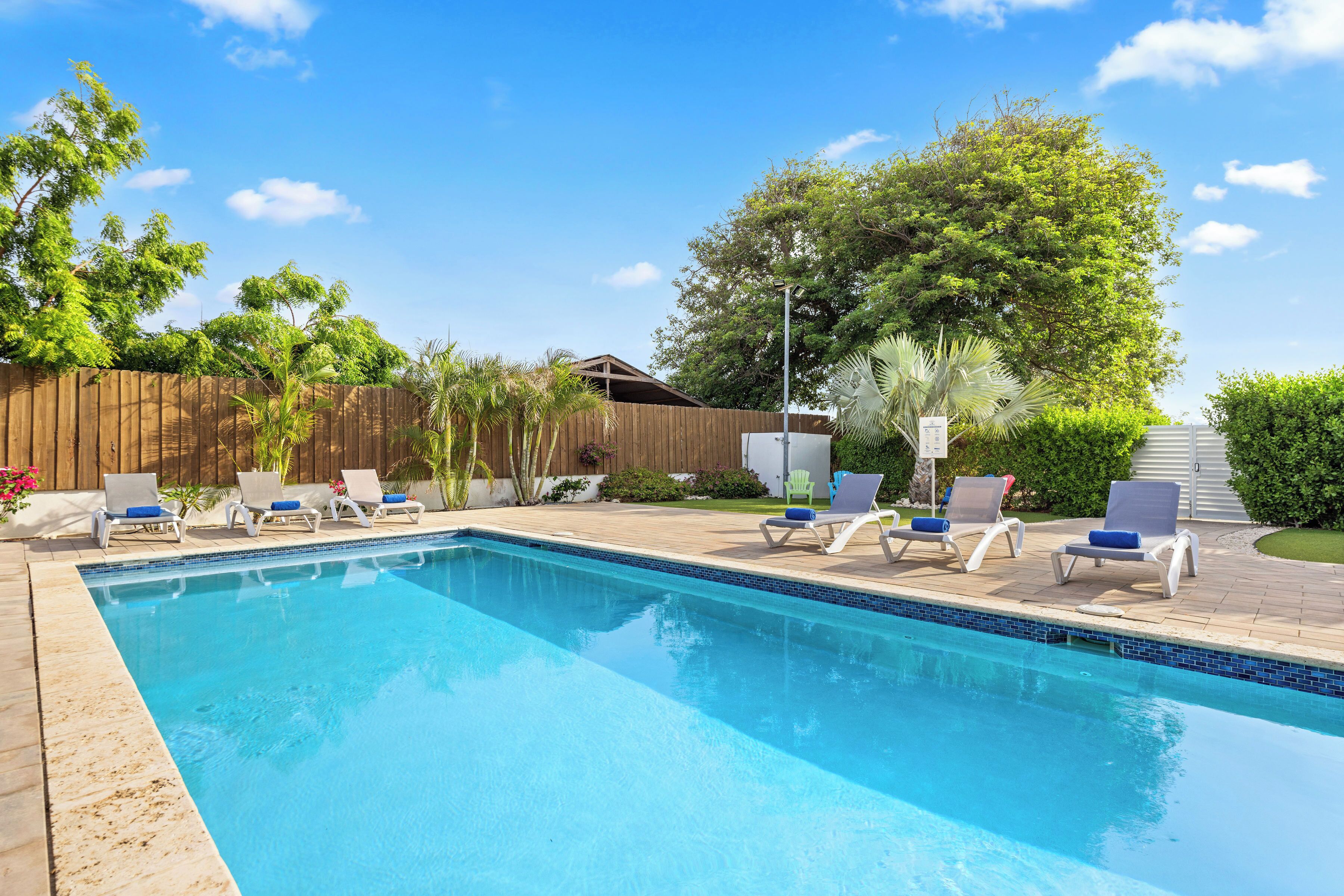 A rectangular swimming pool with a tiled edge, surrounded by lounge chairs with blue cushions.
