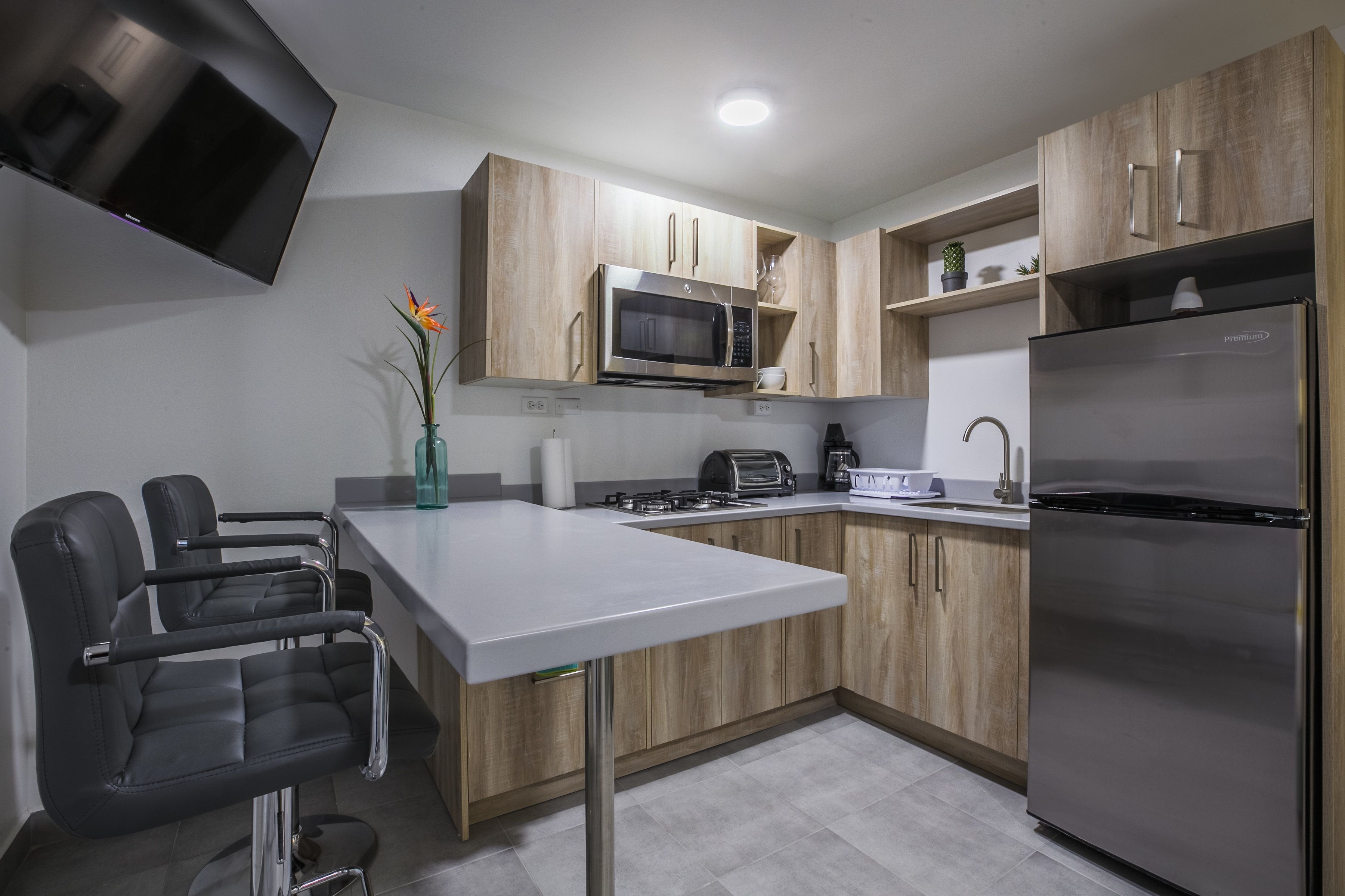 A modern kitchen with wooden cabinets, a stainless steel refrigerator, a microwave, and a built-in gas stove.