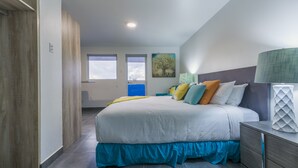 A bedroom with a large bed, a nightstand, a lamp, and a painting on the wall. - Turibana Plaza (Noord)