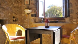 Une pièce aux murs de pierre, une fenêtre donnant sur les arbres, une table avec une lanterne et des chaises en osier.