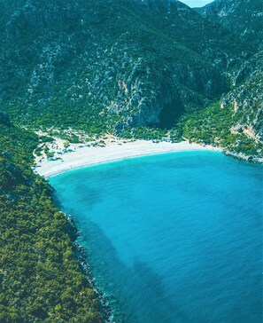 An aerial view of a coastal area with a beach, dense greenery, and rocky terrain.