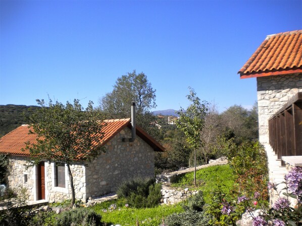 A stone building with a red-tiled roof, surrounded by greenery and a clear blue sky.