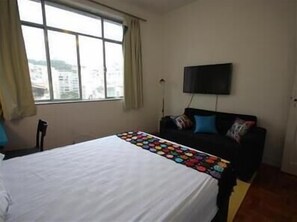 A hotel room with a bed, a TV mounted on the wall, and a window with curtains.