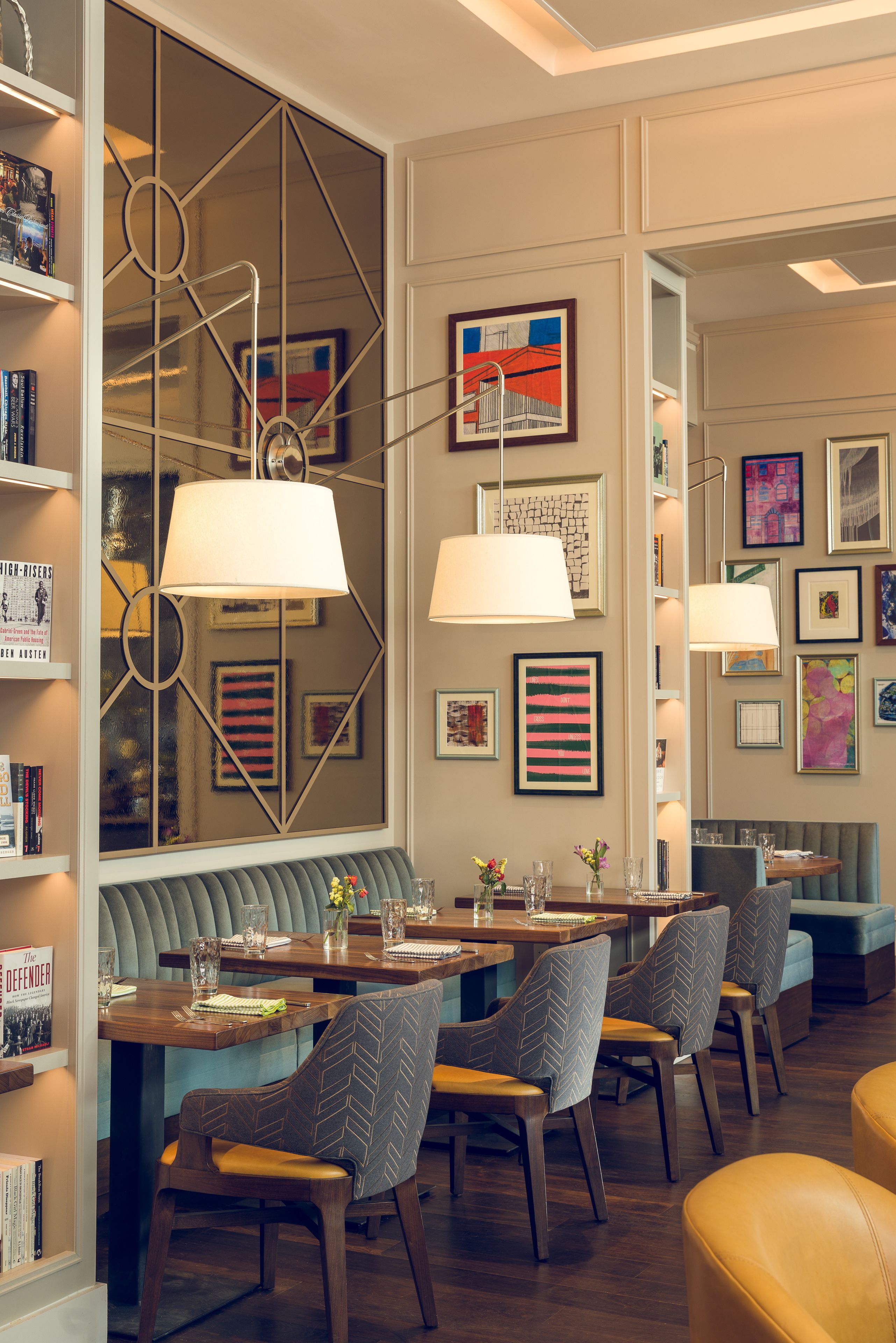 A modern dining area with a wooden table, cushioned chairs, and a bench. There are bookshelves and framed artwork on the walls.