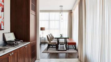 A modern hotel room with a wooden cabinet, a dining area with a table and chairs, and a large window with curtains.