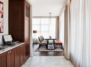 A modern hotel room with a wooden cabinet, a dining area with a table and chairs, and a large window with curtains.