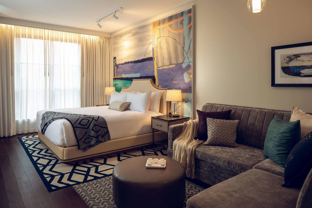 Quarto de hotel com uma cama grande, um sofá, uma mesa de cabeceira e um quadro na parede.
