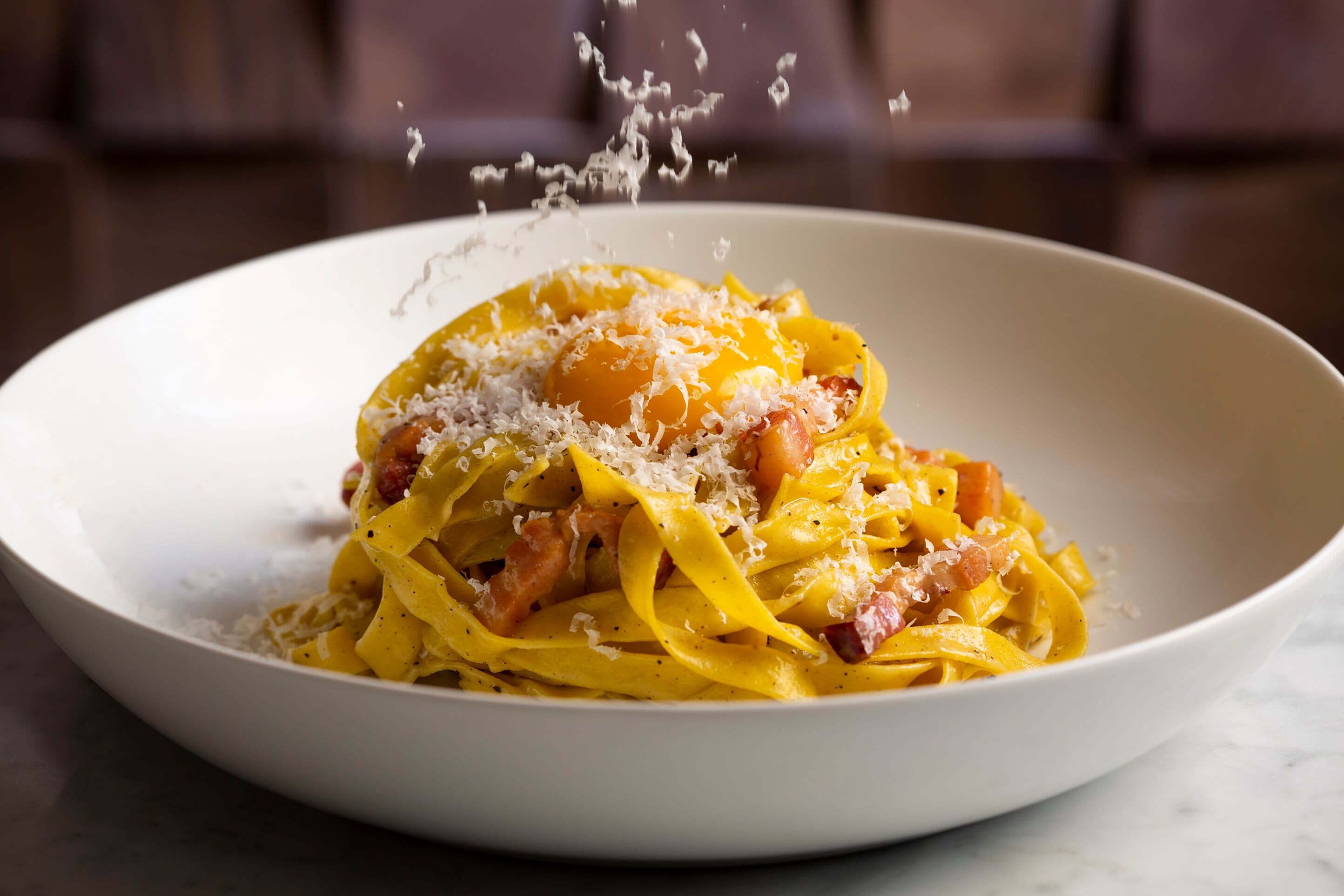 Un plato de pasta con salsa cremosa, decorado con queso rallado y un huevo pochado.