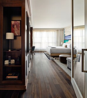 A hotel room with a large bed, a desk with a lamp, a bookshelf, and a painting on the wall.