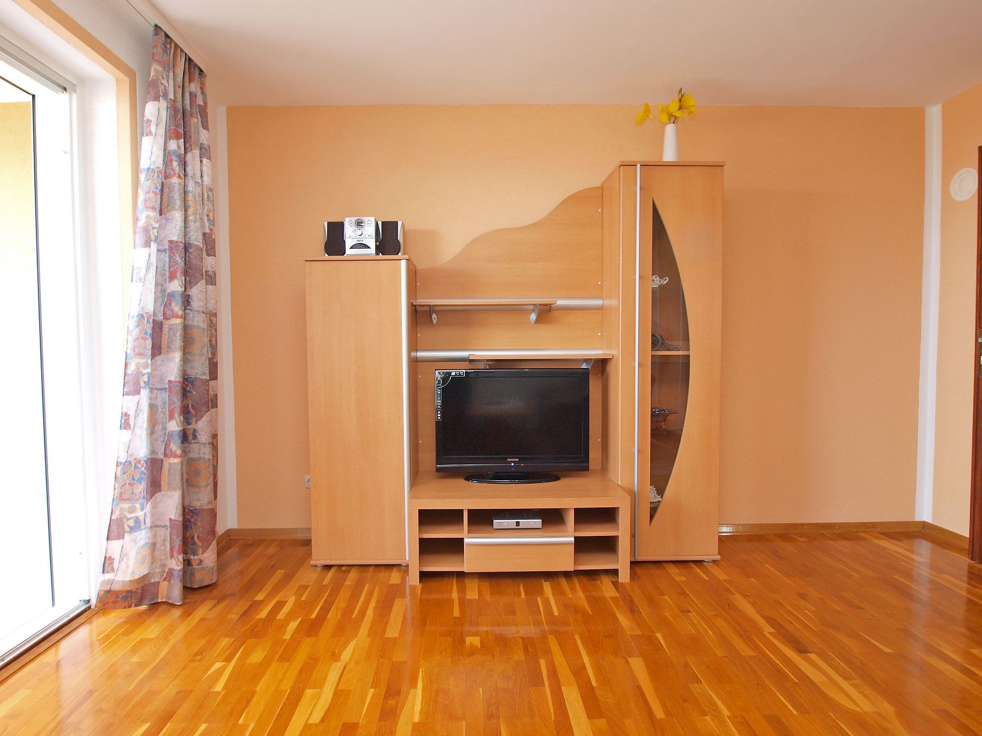 A living room with a wooden entertainment unit, a flat-screen TV, and a vase with flowers.