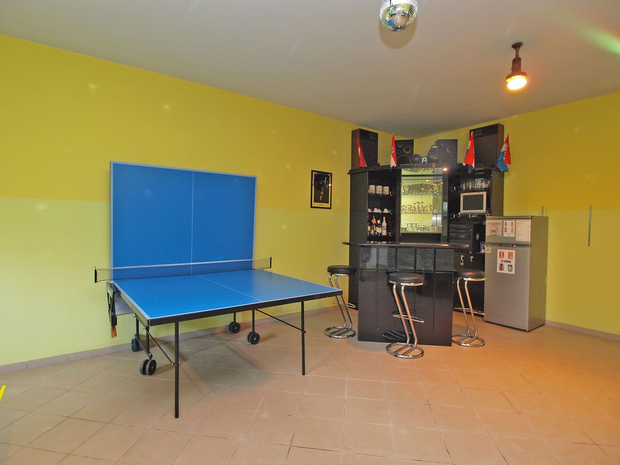 A room with a ping pong table, a bar area with stools, and a refrigerator.