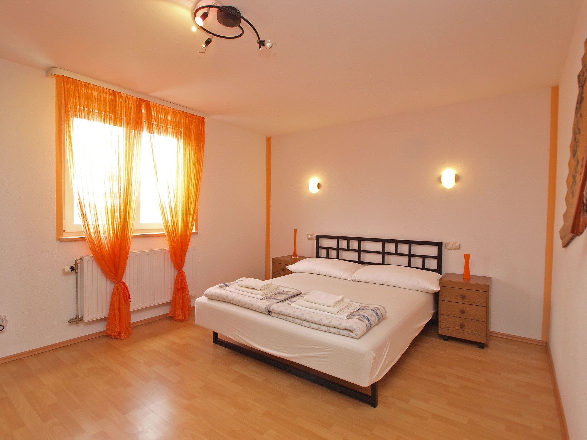 Une chambre à coucher comprenant un lit, deux tables de chevet, une fenêtre avec des rideaux et des lampes fixées au mur.