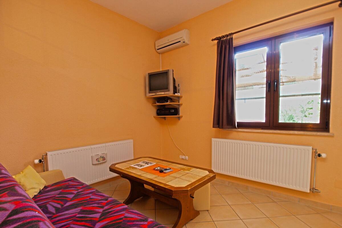 A room with a bed, a small table, a TV, and a window with curtains.